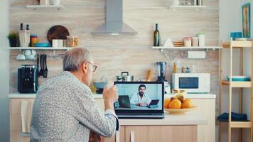 Sénior couple pendant vidéo conférence avec médecin en utilisant portable dans cuisine discuter à propos santé problèmes. en ligne santé consultation pour personnes âgées gens drogues maladie Conseil sur symptômes, médecin télémédecine webcam. médical se soucier l'Internet bavarder video