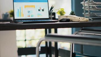 Wheelchair in inclusive office and notebook showing marketing report data. Medical chair in workspace offering accessibility and laptop with business analytics, handheld camera shot video