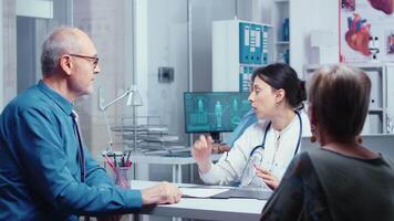 Young woman doctor getting X Ray from nurse while talking with old couple about their problems. Modern hospital or private clinic healthcare checkup for disease prevention and healthcare problems. Patient complaints and medicare insurance video