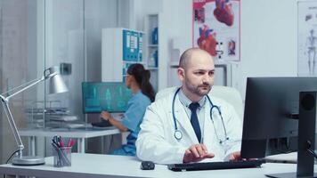 Medical staff working in modern private clinic. Practitioner doctor working on PC while medical staff and nurses are talking with patients behind glass walls. Healthcare system specialist in hospital video