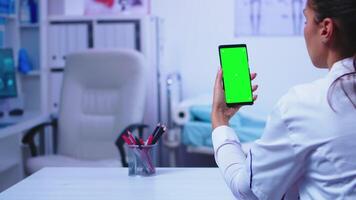 Chroma key display on smartphone used by doctor in clinic cabinet and nurse working on computer. Healthcare specialist in hospital cabinet using smartphone with mockup. video