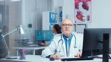 Doctor making an online consultation from private modern clinic where patients are talking with nurses. Medical stuff walking in the background. Using internet technology and offering medical advice video