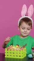 Vertical Video Sweet young boy making colorful arrangements for Easter holiday festivity, putting painted eggs in a handcrafted basket. Ecstatic joyful kid using crafting materials to create decorations. Camera A.