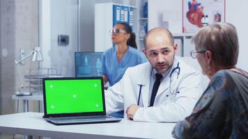 Doctor talking near a laptop with green screen and elderly patient looking at it. Mockup mock-up isolated background ready to be removed chroma key keying for your app or advertisement video