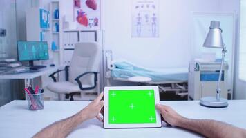 Pov shot of assistant holding tablet pc with green screen in hospital cabinet and doctor wearing white coat working on computer. Medic using tablet with chroma key on display in medical clinic. video