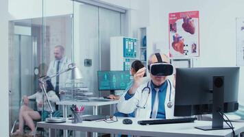 Senior physician using VR glasses in modern private clinic to study diseases in virtual space and modern technology. In the background modern clinic with glass walls and patients with doctors in hallway video