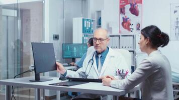 Old experienced practitioner presenting modern X Ray on computer display to young patient. Practitioner explayning medicine computer diagnosis image X Ray. Radiology health care scan analyzing in modern private clinic hospital video