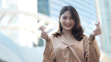 Teenager Asian woman feeling happy smiling and looking to camera while relax at outdoor city space. Portrait of successful business woman showing OK hand and wave up hand. Happy feeling concept. video