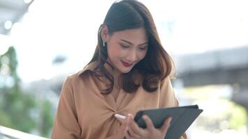 Asian business woman is walking in rush hour at outdoor pedestrian walk way and holding tablet and file working. Concept working life and traveling at outdoor city space. video