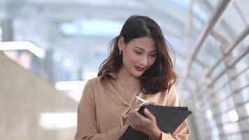 Asian business woman is walking in rush hour at outdoor pedestrian walk way and holding tablet and file working. Concept working life and traveling at outdoor city space. video