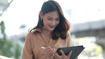 Asian business woman is walking in rush hour at outdoor pedestrian walk way and holding tablet and file working. Concept working life and traveling at outdoor city space. video