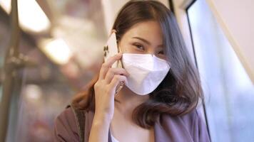 Aziatisch bedrijf vrouw vervelend gezicht masker terwijl op reis in massa doorvoer trein. vrouw is aan het kijken iets Aan slim telefoon met terwijl staand Bij venster. bescherming voor epidemie en Gezondheid in openbaar. video