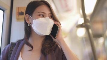 Asian Business Woman wearing face mask while traveling in mass transit train. female is watching something on smart phone with while standing at window. Protection for epidemic and health in public. video