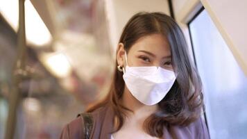 Asian Business Woman wearing face mask while traveling in mass transit train. female is watching something on smart phone with while standing at window. Protection for epidemic and health in public. video