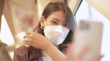 Asian Business Woman wearing face mask while traveling in mass transit train. female is watching something on smart phone with while standing at window. Protection for epidemic and health in public. video