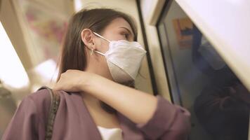 asiatico attività commerciale donna indossare viso maschera mentre in viaggio nel massa transito treno. femmina è Guardando qualcosa su inteligente Telefono con mentre in piedi a finestra. protezione per epidemico e Salute nel pubblico. video