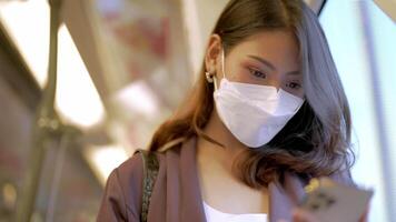 Asian Business Woman wearing face mask while traveling in mass transit train. female is watching something on smart phone with while standing at window. Protection for epidemic and health in public. video