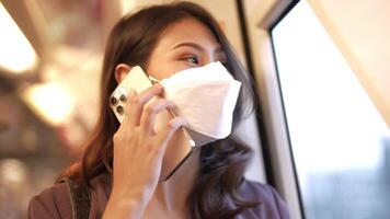 asiatico attività commerciale donna indossare viso maschera mentre in viaggio nel massa transito treno. femmina è Guardando qualcosa su inteligente Telefono con mentre in piedi a finestra. protezione per epidemico e Salute nel pubblico. video