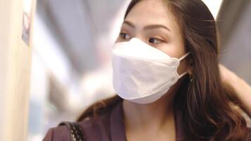 asiatisch Geschäft Frau tragen Gesicht Maske während Reisen im Masse Transit Zug. weiblich ist Aufpassen etwas auf Clever Telefon mit während Stehen beim Fenster. Schutz zum Epidemie und Gesundheit im öffentlich. video