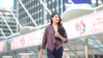 Asian business woman is walking in rush hour at outdoor pedestrian walk way and holding tablet and file working. Concept working life and traveling at outdoor city space. video