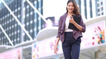 Asian business woman is walking in rush hour at outdoor pedestrian walk way and holding tablet and file working. Concept working life and traveling at outdoor city space. video