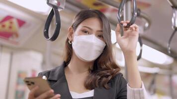 Asian Business Woman wearing face mask while traveling in mass transit train. female is watching something on smart phone with while standing at window. Protection for epidemic and health in public. video