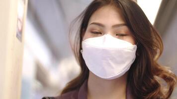 Aziatisch bedrijf vrouw vervelend gezicht masker terwijl op reis in massa doorvoer trein. vrouw is aan het kijken iets Aan slim telefoon met terwijl staand Bij venster. bescherming voor epidemie en Gezondheid in openbaar. video