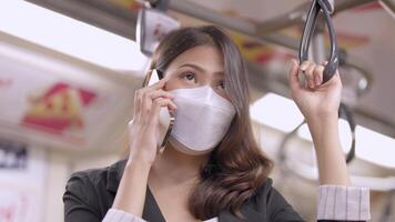 asiatico attività commerciale donna indossare viso maschera mentre in viaggio nel massa transito treno. femmina è Guardando qualcosa su inteligente Telefono con mentre in piedi a finestra. protezione per epidemico e Salute nel pubblico. video