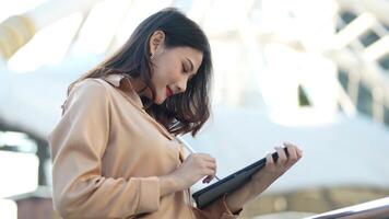 Aziatisch bedrijf vrouw is werken Bij buitenshuis voetganger wandelen manier en Holding tablet en het dossier werken. concept werken leven en op reis Bij buitenshuis stad ruimte. video