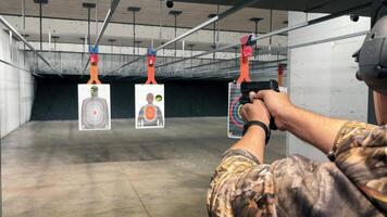 Man Practicing at Indoor Shooting Range, A man in camo attire aiming a handgun at targets in an indoor shooting range. video