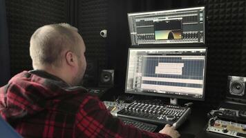 Sound Engineer Working in Recording Studio, A sound engineer with a flannel shirt is mixing audio on professional equipment in a music production studio. video