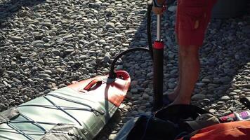 Mens blaast op sta op plas bord. persoon pompen Aan strand dichtbij omhoog schot van pomp en persoon handen in focus terwijl constant pompen. langzaam beweging video