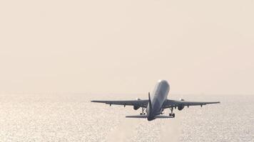 Cinematic footage of a jet plane taking off in the backlight of the shining sea. Airliner climbing, rear view. Plane flying away video