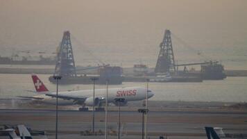 HONG KONG - NOVEMBER 07, 2019. Boeing 777 of SWISS landing, touching and braking at sunset at Hong Kong airport, long shot side view. SWISS is the largest airline in Switzerland video