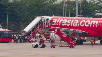 PHUKET, THAILAND - FEBRUARY 27, 2023. Airbus A320 of AirAsia at Phuket Airport. People board an airplane. Airplane on the airfield, stairway. Travel concept video