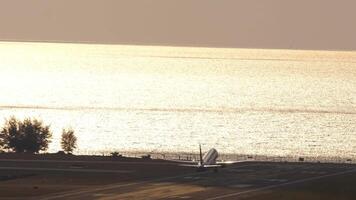 Airplane silhouette climbing after takeoff over the sea in backlight, rear view, long shot video