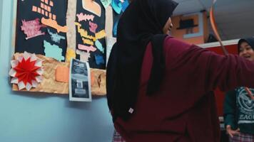 Person in a hijab pointing at a bulletin board with various flyers and notices. video