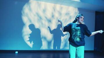 Person dancing in a room with blue lighting and a large shadow projected on the wall behind. video