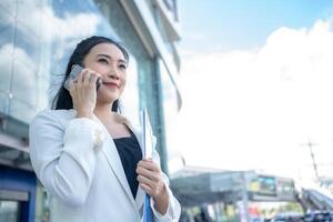 Young businesswoman holding coffee hot cup and using a smartphone while walking through the city photo