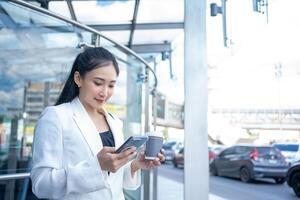 Young businesswoman holding coffee hot cup and using a smartphone while walking through the city photo