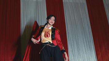 Performer in red jacket posing on stage with curtains in the background. video