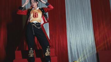 Performer in a red jacket on stage with dramatic lighting and curtains in the background. video