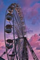 Silhouette of a Ferris wheel against a vibrant sunset sky with pink and purple clouds. photo