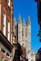 Gothic cathedral towers over historic city street under clear blue sky in Canterbury, England. photo