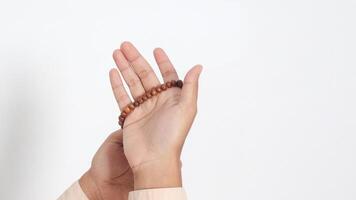 Close up hand of religious Asian muslim man in koko shirt with skullcap praying earnestly with his hands raised, holding islamic beads. Devout faith concept. Isolated image on white background photo