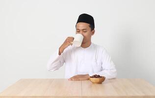 Portrait of serious Asian muslim man drinking a glass of water during sahur and breaking fast. Culture and tradition on Ramadan month. Isolated image on white background photo