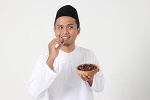 Portrait of excited Asian muslim man eating date fruit during sahur or breaking the fast. Culture and tradition on Ramadan month. Isolated image on white background photo