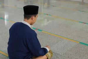 Portrait of religious Asian man in muslim shirt praying and doing salat or sholat in mosque photo