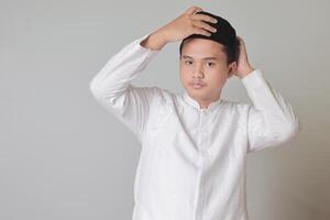 Portrait of Asian muslim man trying to wear songkok or black skullcap. Isolated image on white background photo