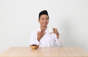 retrato de grave asiático musulmán hombre Bebiendo un vaso de agua durante sahur y rotura rápido. cultura y tradicion en Ramadán mes. aislado imagen en blanco antecedentes foto